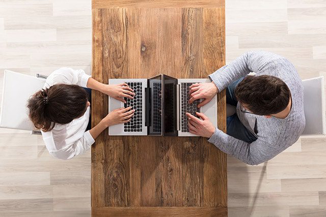 two people facing each other at a table but looking at their laptops instead